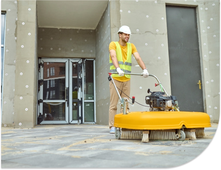Worker in construction vest operating an industrial floor scrubber outside a recently constructed building.