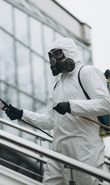 Technician in hazmat gear spraying pesticide in an industrial space, representing environmental risk control.