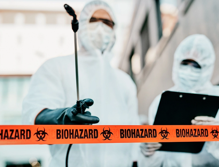 Technicians in full protective suits standing behind biohazard tape, preparing for hazardous sanitation work.