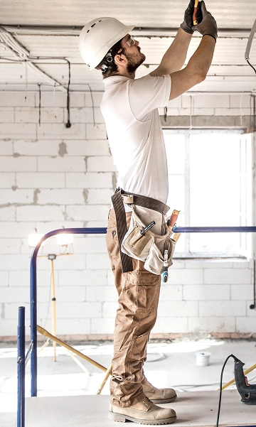 Electrician on ladder working on overhead lighting system inside a commercial facility.