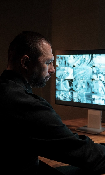 Man monitoring security feeds on screens, symbolizing professional on-site security presence.