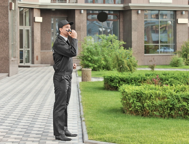 Security guard patrolling facility exterior and speaking into a walkie-talkie, illustrating active perimeter surveillance.