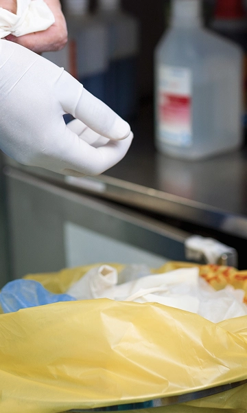 Gloved hands safely disposing of sharp medical waste into a compliant container.
