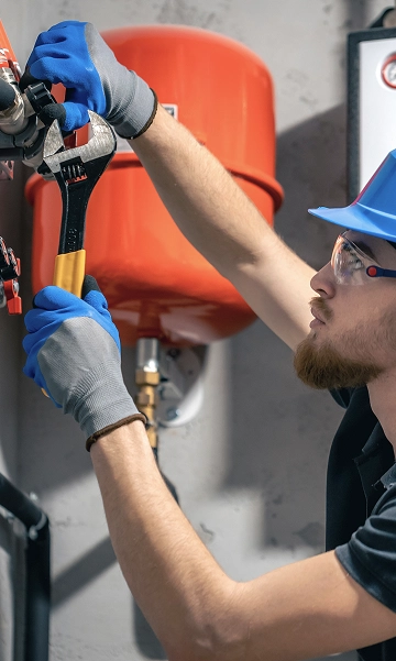 Plumber using wrench on red pipe system, performing maintenance on commercial plumbing.