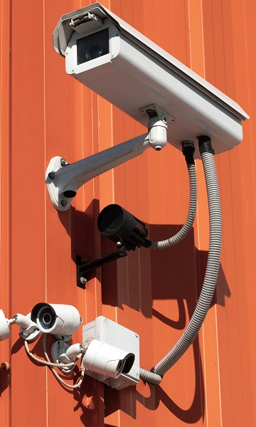 Outdoor surveillance camera mounted on an orange wall, representing full-angle video monitoring.