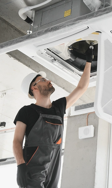 “Technician in hard hat inspecting HVAC ductwork for air quality and seasonal maintenance.”